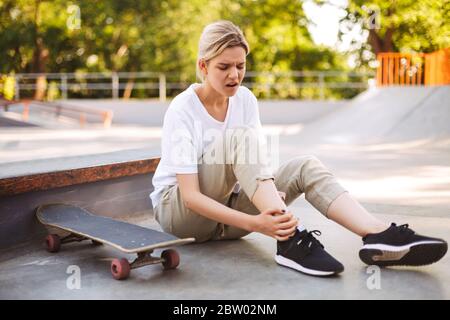 Verärgert Skater Mädchen hält ihr schmerzhaftes Bein mit Skateboard in der Nähe, während Zeit am Skatepark Stockfoto