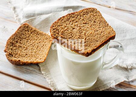 Ein Glas fermentierter gebackener Milch und Scheiben Schwarzbrot auf einem rustikalen Holztisch. Traditionelles Frühstück Stockfoto