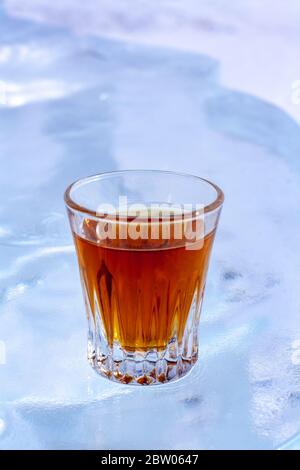 Ein Glas Whiskey steht auf einem weißen Hintergrund aus Eis. Orangengetränk im Glas. Ansicht von oben von der Seite. Für Werbung für alkoholische Getränke. Stockfoto