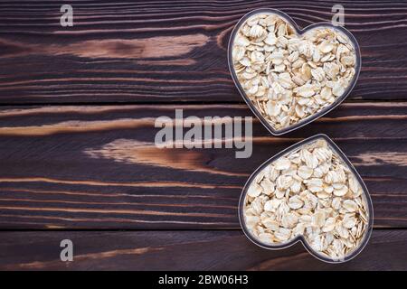 Müsli in Schale Herz auf dunklem natürlichen Holzbrett Hintergrund geformt. Roher Haferbrei. Leerer Platz, kopieren Sie Platz für Text Stockfoto