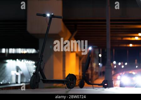 Nahaufnahme von Black Electric Kick Scootern im Stadtbild bei Nacht. Kick Roller in der Nähe vorbei Autos auf Urban Hintergrund Stockfoto