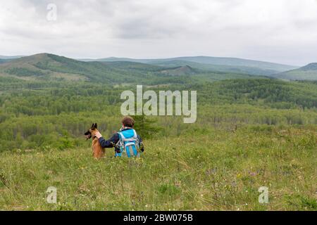 Rückansicht eines Mannes mit einem Hund, der auf einem Hügel sitzt. Das Konzept der Liebe für Haustiere und Reisen. Stockfoto