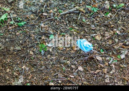 Blaue Einweg-medizinische Maske liegt auf dem Boden im Wald zwischen trockenen Blättern und kleinen Holzstücken, Umweltverschmutzung in Zeiten der Spre Stockfoto