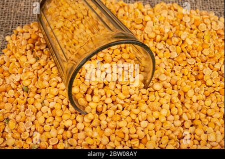 Gelbe Erbsen in einem geschnittenen Glas und grittert auf einem Hintergrund von grob-strukturierten Burlap verstreut. Traditionelles Getreide für die Herstellung von Suppen und Porridge. Clo Stockfoto