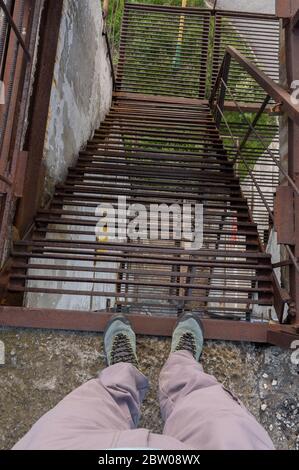 Abstieg entlang der eisernen Treppe. Menschliche Füße am Treppenrand. Blick von oben. Stockfoto