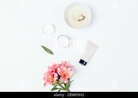 Floral flach legen Zusammensetzung Set von grundlegenden Hautpflegeprodukten, Reiniger, hausgemachte Maske und kosmetische Creme neben rosa Blüten auf weißem Hintergrund. Stockfoto