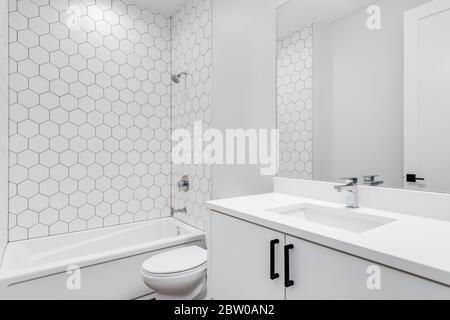 Ein schlichtes weißes Badezimmer mit Sechskant-Keramikfliesen, die die Wand um die Wanne herum säumen. Stockfoto