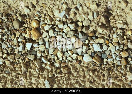 Kleine Steine auf dem Sand. Das Ufer des Stausees von Kieselsteinen, Schutt. Meer felsiger Strand. Die Textur von Stein und Sand. Der Hintergrund für das Design und der Ort für den Text. Stockfoto