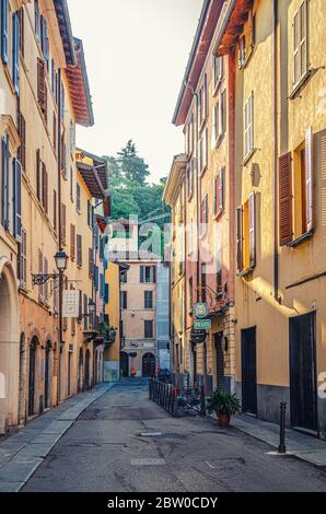 Brescia, Italien, 11. September 2019: Typisch italienische Straße mit alten bunten Gebäuden mit Fensterläden, Straßenbeleuchtung an der Wand, Restauranttische, historisches Zentrum, vertikale Ansicht, Lombardei Stockfoto