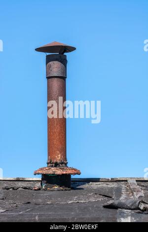 Alte rostige Eisenschornstein auf dem Dach eines zerstörten Hauses gegen den blauen Himmel. Stockfoto