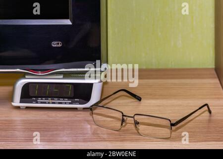 Die Gläser, die auf der hölzernen Oberfläche neben der elektronischen Uhr liegen. Stockfoto