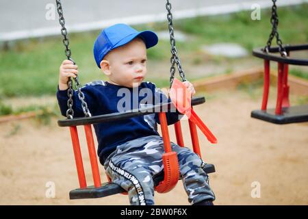 Schönes Kind, das auf einer Schaukel reitet und Spielzeug in den Händen hält Stockfoto