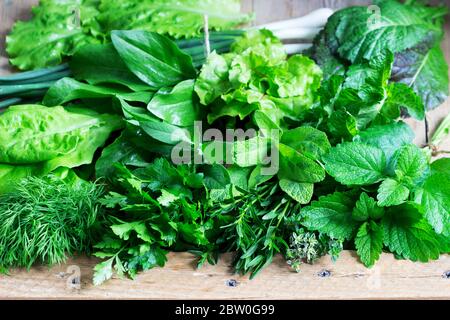 Eine Vielzahl von würzigen Kräutern, Salat und grünen Zwiebeln auf einem hölzernen Hintergrund. Rustikaler Stil. Stockfoto
