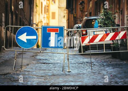 Straßenbauarbeiten führen zu Umgehung der Straßenschilder. Sackgasse und Pfeil links abbiegen. Eisenkugelsperre. Straße mit Pflastersteinen. Stockfoto