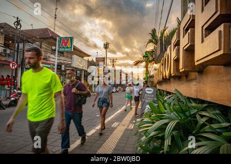 Ubud, Bali, Indonesien - 10. Mai 2018: Belebte Ubud Hauptstraße bei Sonnenuntergang mit Touristen im Vordergrund und mit Nahaufnahme eines Starbucks Kaffee si Stockfoto