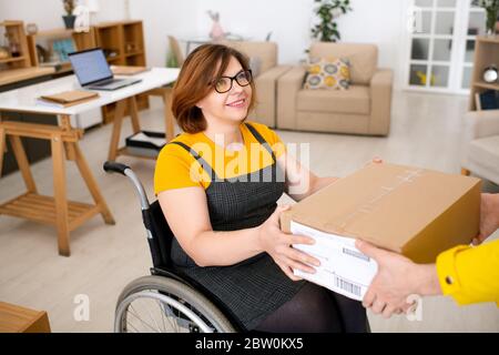 Unkenntlich LieferungMann geben Paket an zufriedene behinderte Frau im Rollstuhl Stockfoto