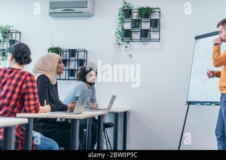 Multiethnische Geschäftsgruppe, die einem Redner zuhört, während sie an einem Geschäftsseminar in einem modernen Workshop teilnimmt. Stockfoto