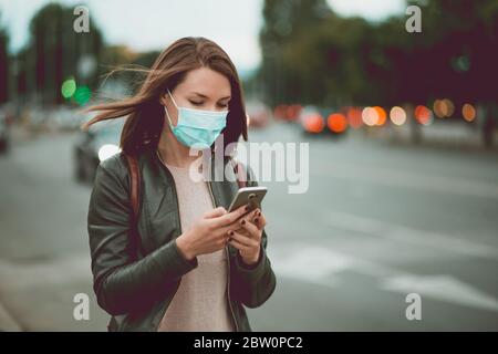 Junge Frau mit Smartphone in der Stadt trägt Gesicht Maskenschutz für Virus covid-19 Stockfoto
