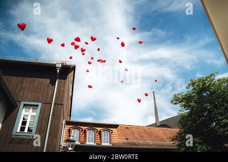 Romantische Aufnahme von roten Liebe Herz Ballons steigt in den Himmel. Gruppe von ins Leben gerufenen Helium aufgeblasen Ballons über dem Dach des Gebäudes. Stockfoto