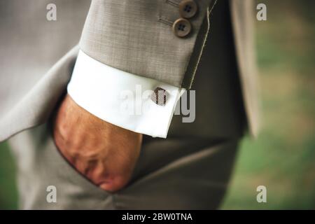 Männliche Hand in der Tasche. Mann in grauem Business-Anzug und weißem Hemd mit quadratischen Manschettenknöpfen. Hintergrund im Freien. Stockfoto