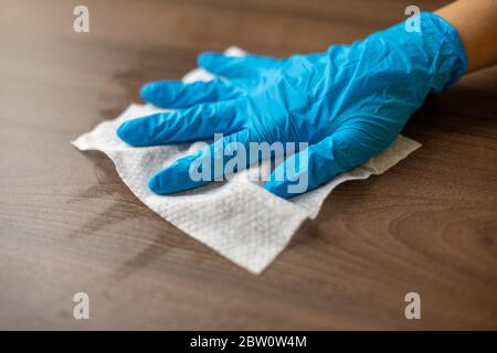 Die Hand der Frau in blauen Handschuhen desinfiziert Reinigung Home Office Holz Tischoberfläche mit feuchten Wischtüchern Stockfoto