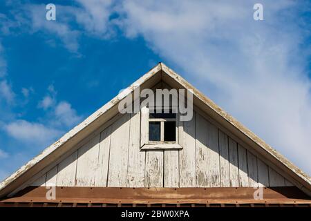 Das Dach eines alten Holzhauses mit einem Fenster gegen den Himmel. Stockfoto