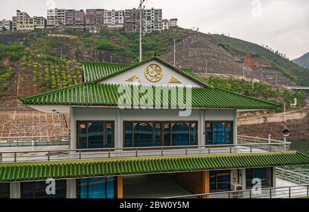 Wushan, Chongqing, China - 7. Mai 2010: Wu-Schlucht im Jangtze-Fluss. Fährterminal mit grünem Dach und goldenem Emblem. Hohe Gebäude auf der Spitze des Hangs un Stockfoto