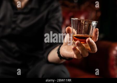 Männliche Hand hält ein Glas Elite-Alkohol, in einem schwarzen Hemd, Nahaufnahme, Studio-Licht Stockfoto