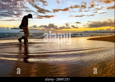 Ein Fischer geht bei Sonnenaufgang am Wasser entlang Stockfoto