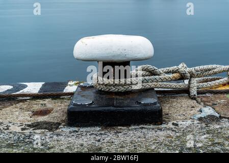 Weißer Poller auf einem Dock mit Festmachen um ihn herum. Wasser im Hintergrund. Lange Belichtung Stockfoto