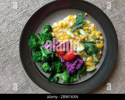 Indonesisches Maismehl mit Brokkoli, Tomaten und in Scheiben geschnittenem ​​purple-Kohl auf dem Teller serviert Stockfoto