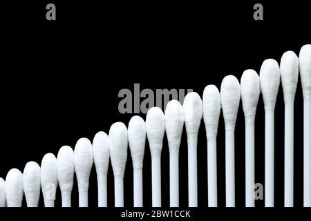 Weiße Wattestäbchen sind auf eine geordnete und schöne Weise auf schwarzem Hintergrund angeordnet. Stockfoto