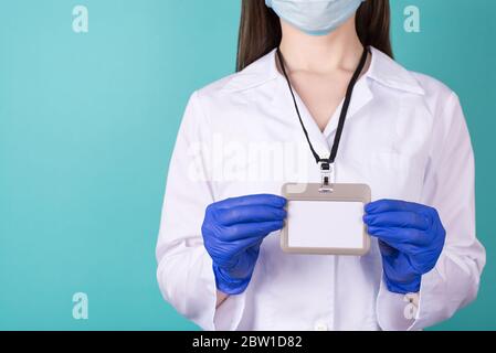 Nahaufnahme beschnittenes Foto von Ärztin in weißem Mantel Gefahr Uniform Handschuhe mit einem leeren Maok bis Namensschild isoliert auf blauem Hintergrund Stockfoto