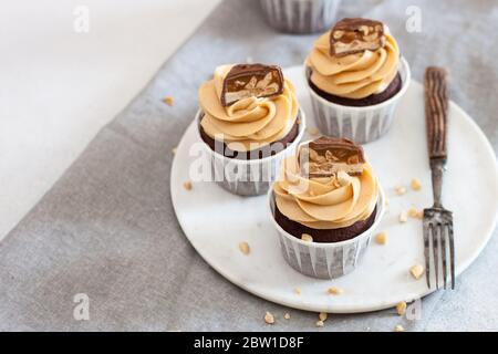 Erdnussbutter Cupcakes mit Schokoladenstückchen und gehackten Nüssen auf grauer Leinentischdecke. Schokoladenteig und Mascarpone-Zuckerguss. Stockfoto