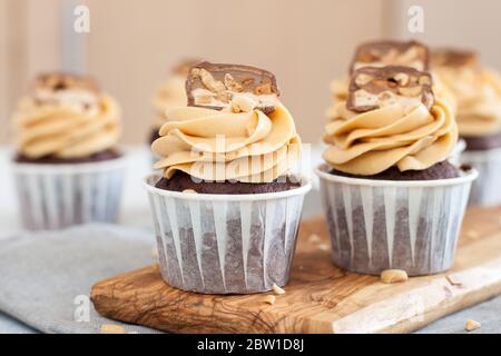 Erdnussbutter Cupcakes mit Schokoladenstückchen und gehackten Nüssen auf grauer Leinentischdecke. Schokoladenteig und Mascarpone-Zuckerguss. Stockfoto