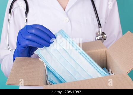 Konzept der humanitären Hilfe. Nahaufnahme beschnittenes Foto von Ärztin in blauen Latex-Handschuhe, die Maske aus offener, unverpackter Schachtel isol nehmen Stockfoto