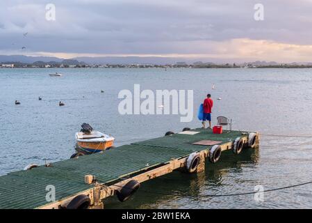 San Juan, Puerto Rico - 30. April 2019: Ein eingefelschiger Fischer steht auf einem Pier mit einem Fischernetz während des Sonnenuntergangs in San Juan, Puerto Rico, Karibik. Stockfoto