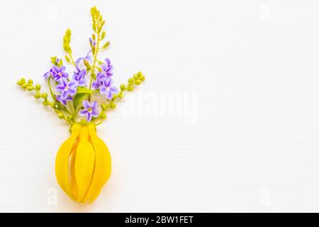 Gelbe Blume Ylang Ylang mit lila Flora lokale Flora von asien Anordnung flach legen Postkarte Stil auf Hintergrund weiß Holz Stockfoto