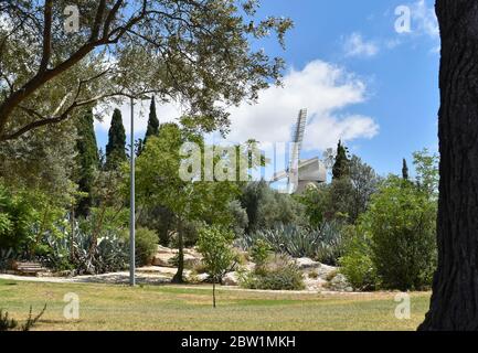 Die alte historische montefiore Windmühle, umrahmt von Bäumen in einem schönen leeren Park in jerusalem israel an einem teilweise bewölkten Frühlingstag während des Covid Stockfoto