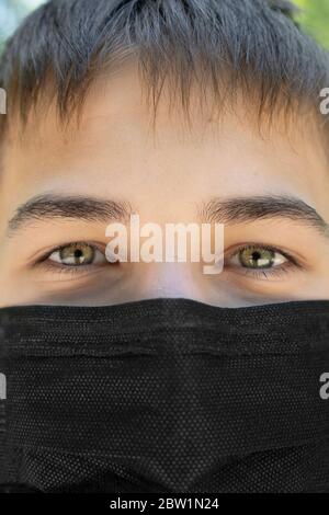 Nahaufnahme schwarze medizinische OP-Maske auf dem Gesicht eines traurigen jungen Mannes. Coronavirus Angst Konzept Stockfoto