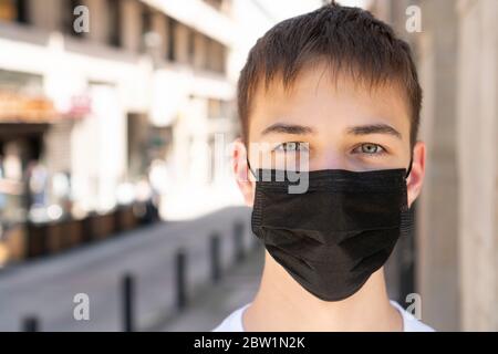 Trauriger junger Mann in einer medizinischen schwarzen Maske nahe der Straße auf einer leeren Stadtstraße ohne Menschen. Allein. Copyspace. Nahaufnahme. Das Konzept des Coronavirus und Stockfoto