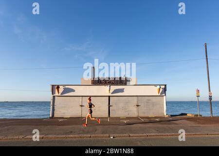 Southend-on-Sea, Großbritannien. Mai 2020. Ein Jogger am frühen Morgen läuft an einem geschlossenen Café am Meer vorbei. Klarer Himmel und warme Luft beginnen am Freitagmorgen in Southend-on-Sea-Sea. Penelope Barritt/Alamy Live News Stockfoto