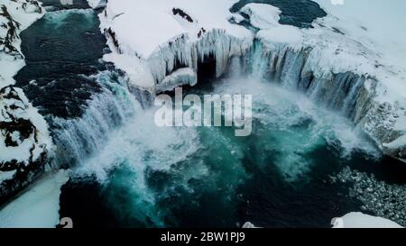 Luftaufnahme eines breiten, aber nicht hohen Wasserfalls in Island. Der Wasserfall ist teilweise gefroren und die Landschaft ist mit Schnee und Eis bedeckt. Die Drohne nahm Stockfoto