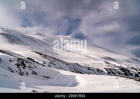 Ein sanft aufgetauter Berg, der diskret seinen Weg zum Himmel findet, wo er auf die dunklen Wolken trifft. Die Sonne trifft den Berg aus dem Rahmen. Stockfoto