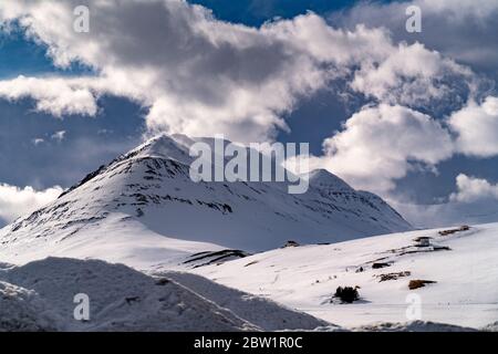 Ein langer und hoher Berg, der zu den Wolken aufsteigt, mit der Sonne auf der einen Seite, und die andere Seite schattete. Ein kleines Haus ist in der Nähe zu sehen. Stockfoto
