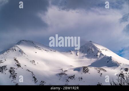 Moody Aufnahme von zwei Gipfeln eines großen Berges in Nordisland. Die Gipfel sind teilweise wolkenbedeckt, und Schnee weht kräftig von ihnen. Das b Stockfoto