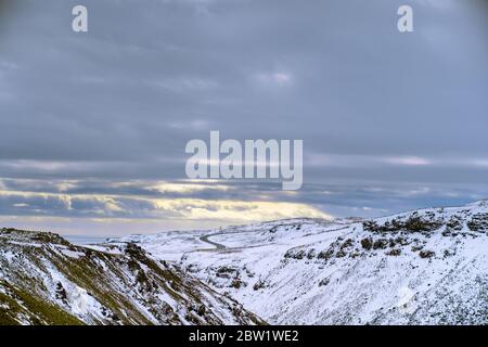 Landschaftsaufnahme von verschneiten Bergen mit Straße im Hintergrund und Dramatische Wolken Stockfoto