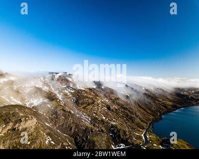 Wolkenbedeckte Berggipfel neben einem See mit einem Kleine Straße durch die Berge Stockfoto