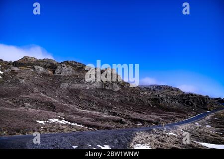 Der Gipfel eines kleineren Berges mit Wolken bedeckt Teile der Berge, und eine einsame Straße Stockfoto