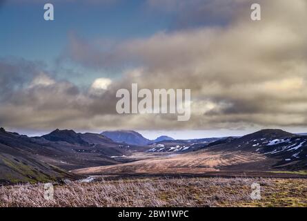 Dramatische isländische Landschaft mit einem alten Farmfeld und teilweise wolkenbedeckten Berggipfeln Stockfoto